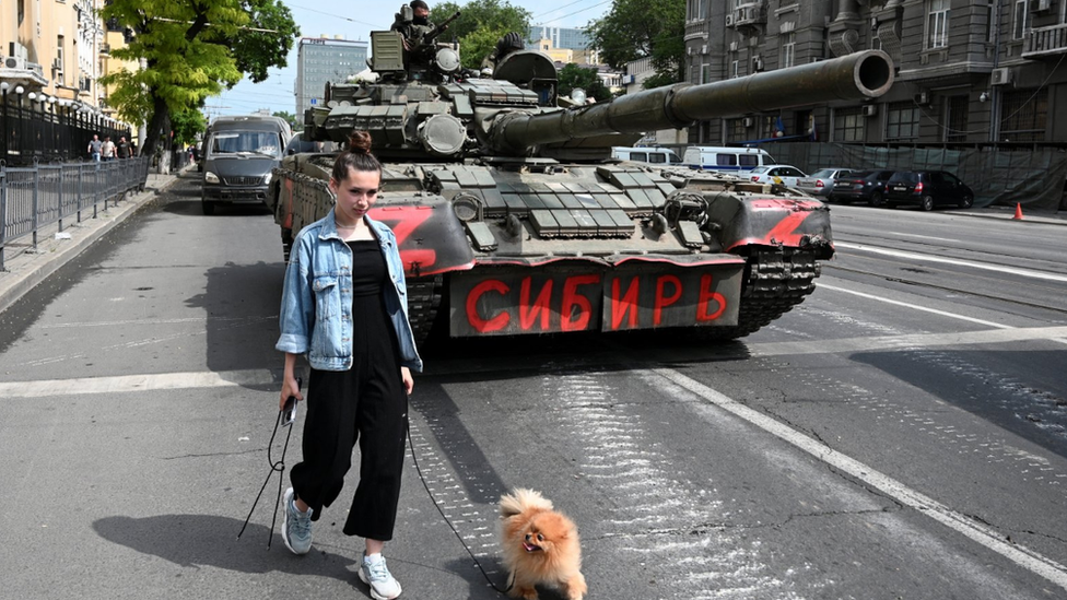 A woman with a dog walks past a tank as fighters of Wagner private mercenary group are deployed in a Rostov-on-Don street near the headquarters of the Southern Military District