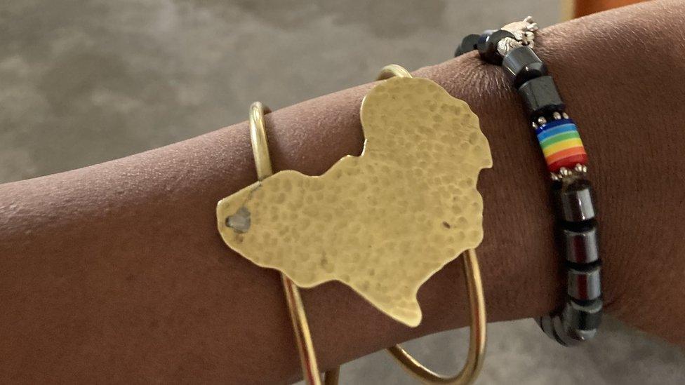 The arm of the member of the queer-affirming church with a bracelet of Africa and a beaded one including an LGBT rainbow