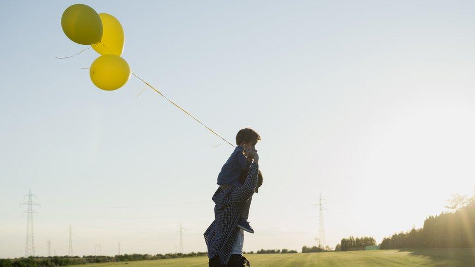 A man with a boy on his shoulders, holding balloons