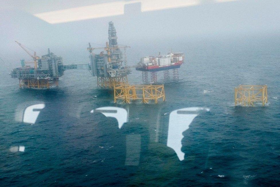 People sitting in a helicopter are reflected in its window as they wait to land at the Johan Sverdrup oil field in the North Sea outside of Norway.