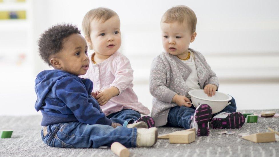 Three nursery-aged children sit playing