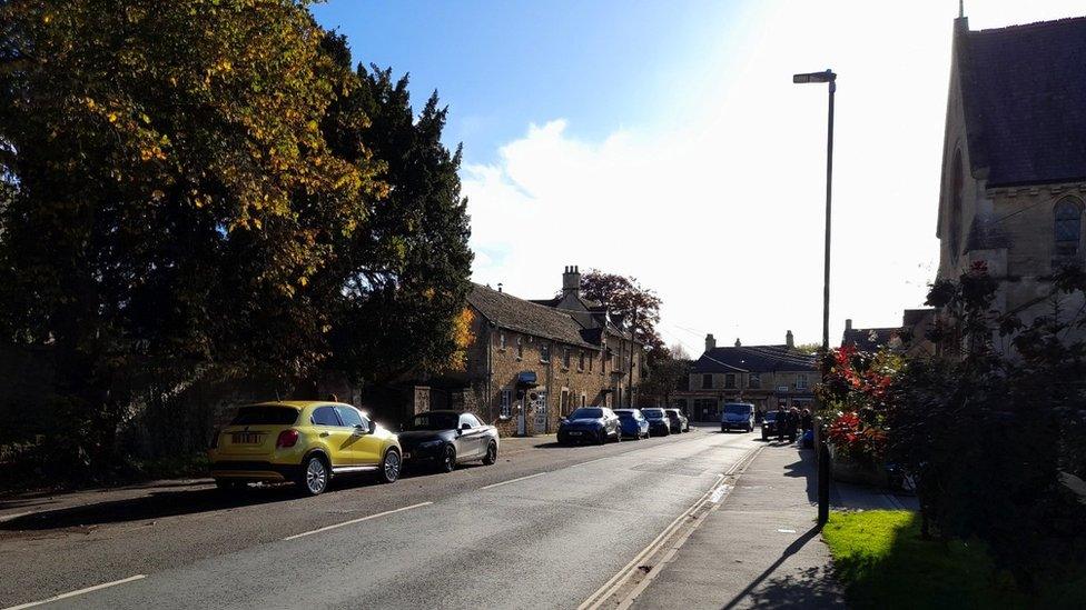 Station Road in Bourton-on-the-Water. It is a narrow street with cars parked along either side of the road.