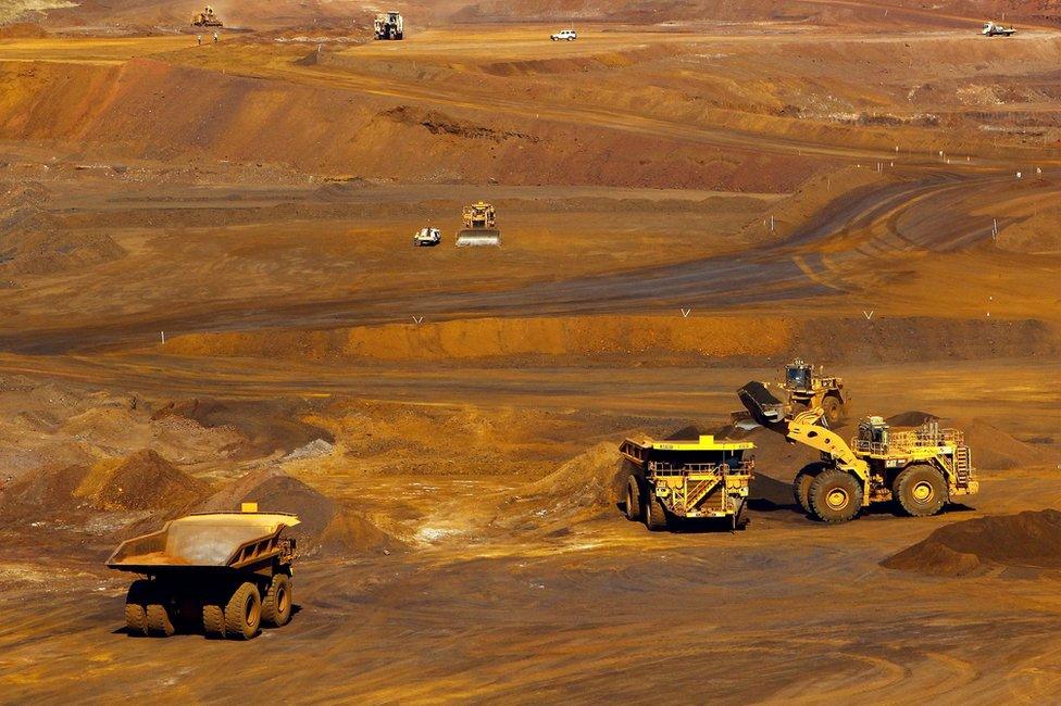 Workers stand around a vehicle as a truck is loaded with iron ore at the Fortescue Metals Group