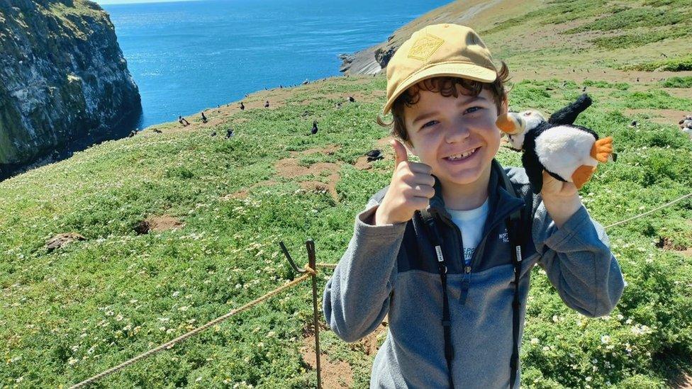 joshua smiling with his thumbs up to the camera while holding a toy puffin