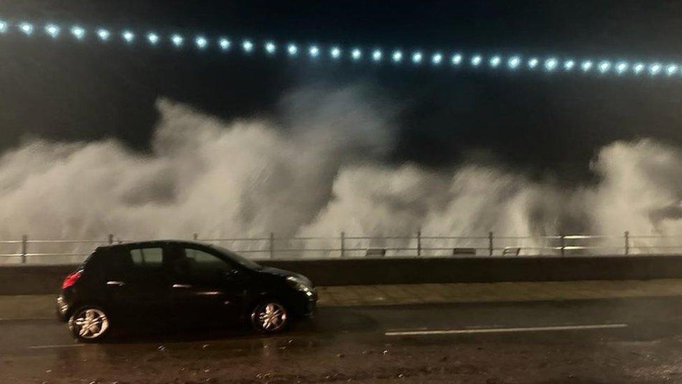 Waves crash into Penzance promenade in Cornwall as a car drives by