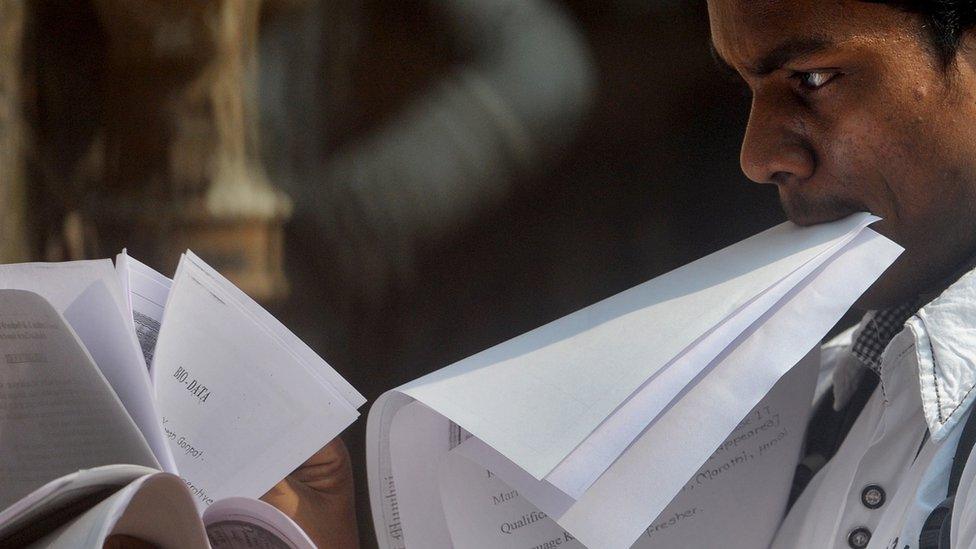 An Indian youth looks through papers as he stands in a queue to apply for a job at a jobs fair in Mumbai on October 12, 2011.