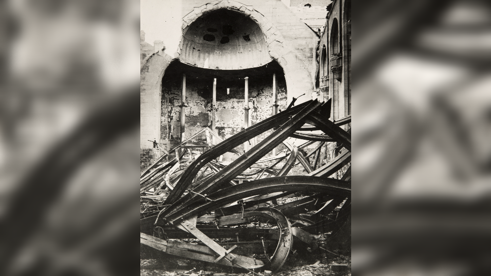 A black and white photo of rubble and steel beams from the ceiling of the great hall which has collapsed onto the floor after being hit by a bomb