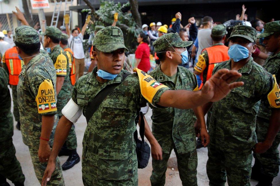 Soldiers stand guard near a collapsed building