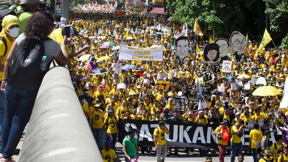 Protesters wearing yellow shirts in Kuala Lumpur hold up cartoons