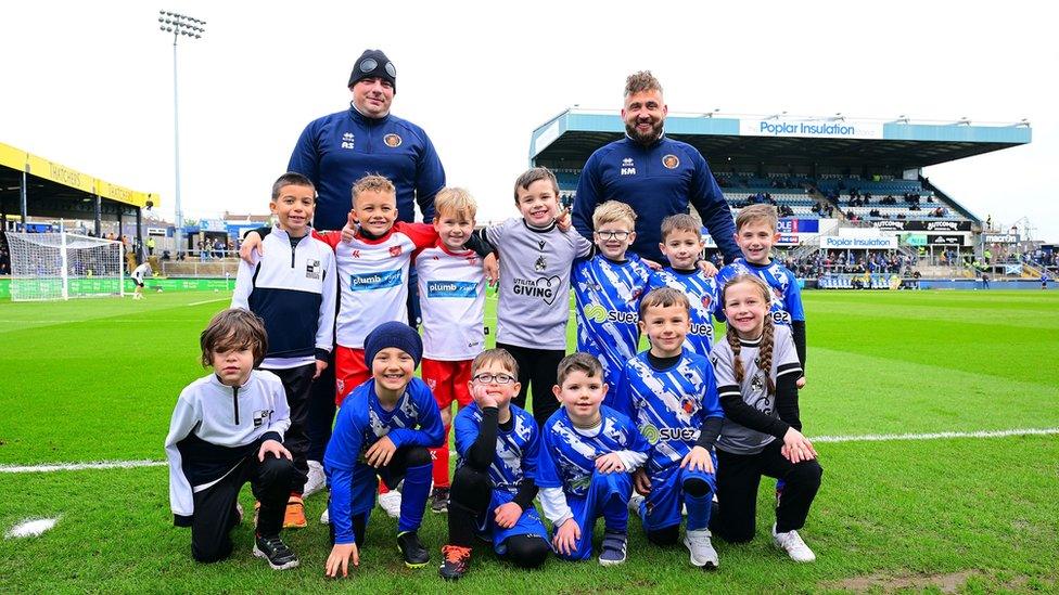 A group of young Bristol Rovers fans face the camera with the Memorial Stadium in the background