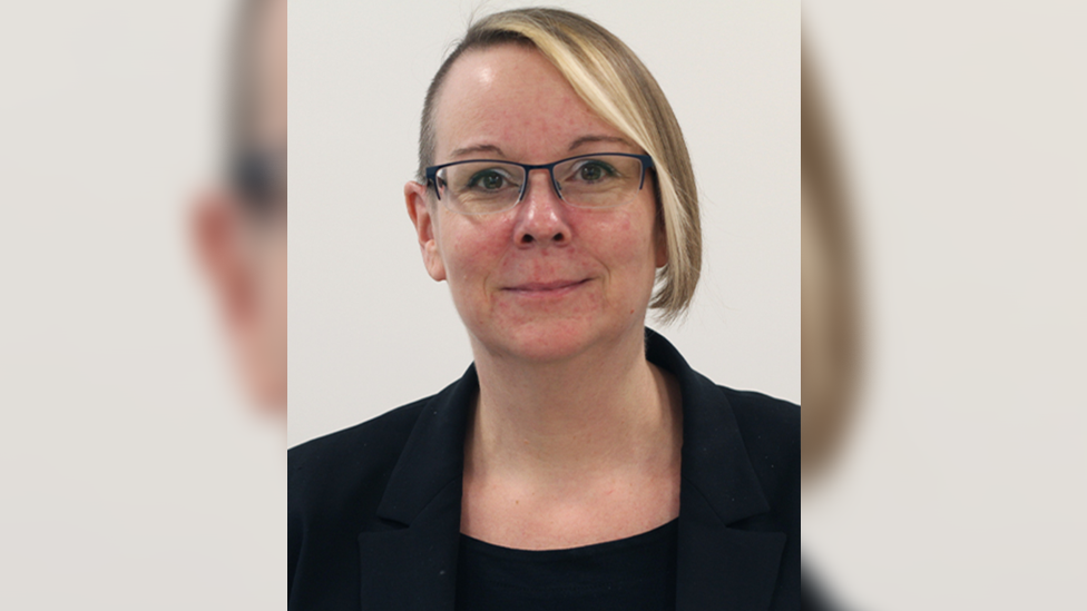 Alexandra Vincent looks at the camera, smiling, wearing glasses and a black jacket