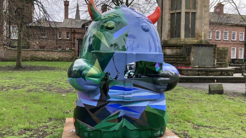 Blue and green shiny Snook standing on grass near a church in York