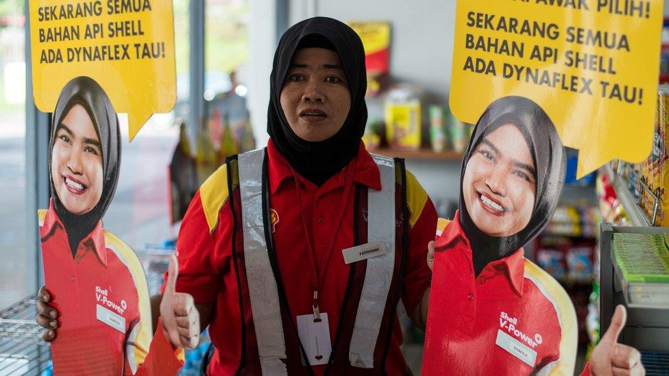 A Shell petrol station employee holds up life-sized cutouts depicting a female staff member, pictured in uniform with a black Muslim headscarf and placed beside individual self-serve petrol pumps as part of a promotional campaign, as they were pulled from display at a Shell station in Bentong, some 70 kms north of Kuala Lumpur in nearby Pahang state on July 4, 2017