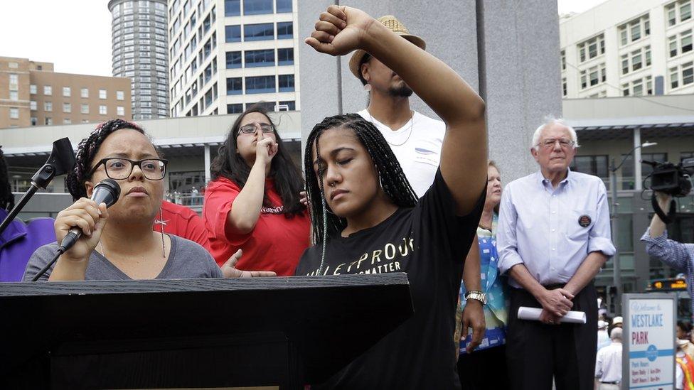 Marissa Johnson, left, speaks as Mara Jacqueline Willaford holds her fist overhead and Democratic presidential candidate Sen. Bernie Sanders, I-Vt., stands nearby as the two women take over the microphone at a rally Saturday, Aug. 8, 2015, in downtown Seattle.