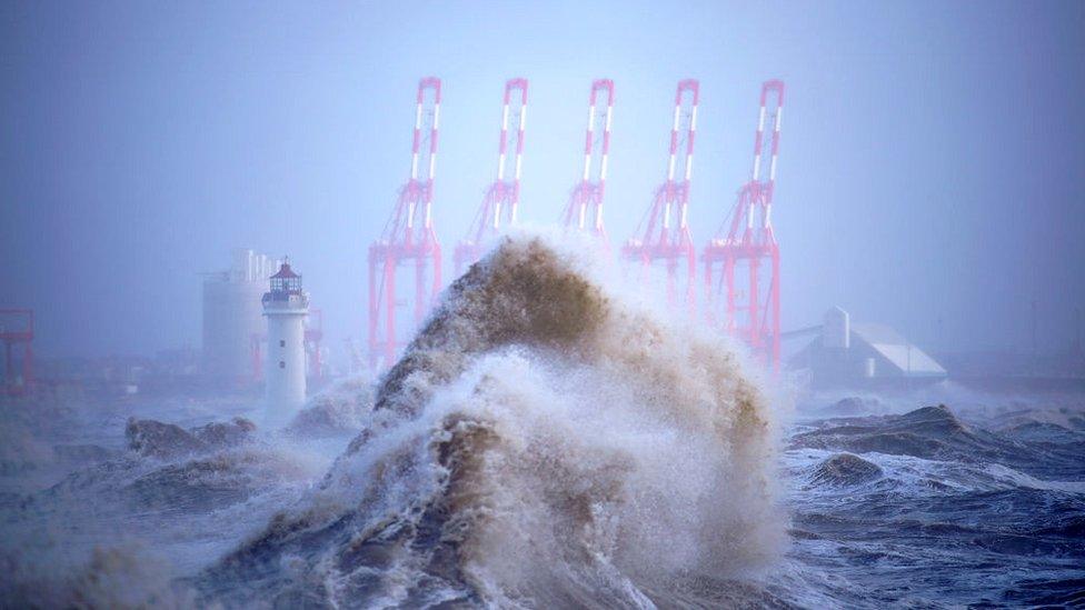 A huge wave with cranes and a light house in the background