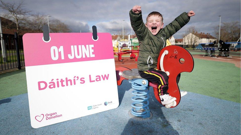 Dáithí Mac Gabhann celebrates on a play park seat with a sign that reads 01 June Dáithí's Law