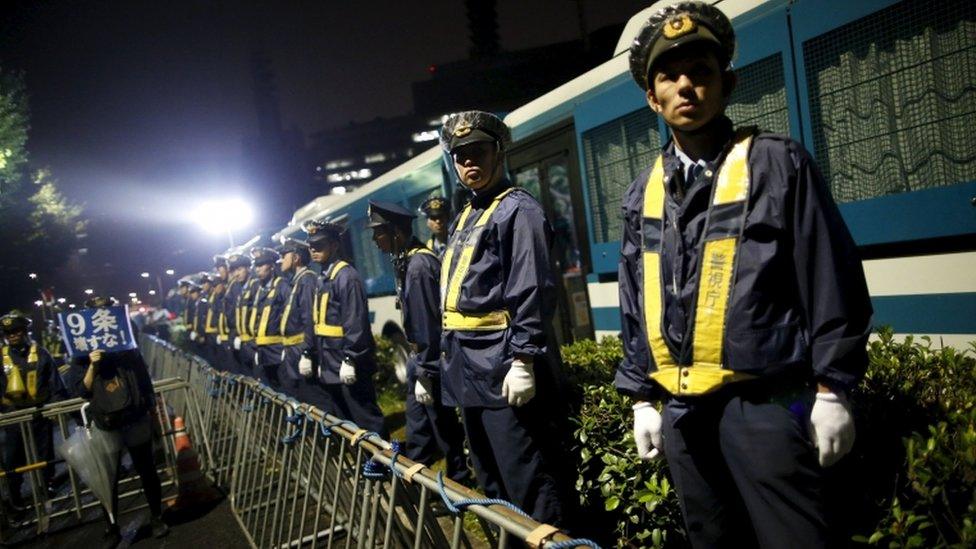 A protester (L) holds a placard as police officers stand guard during a rally against Japan's Prime Minister Shinzo Abe's security bill and his administration in front of the parliament in Tokyo, on 19 September 2015.