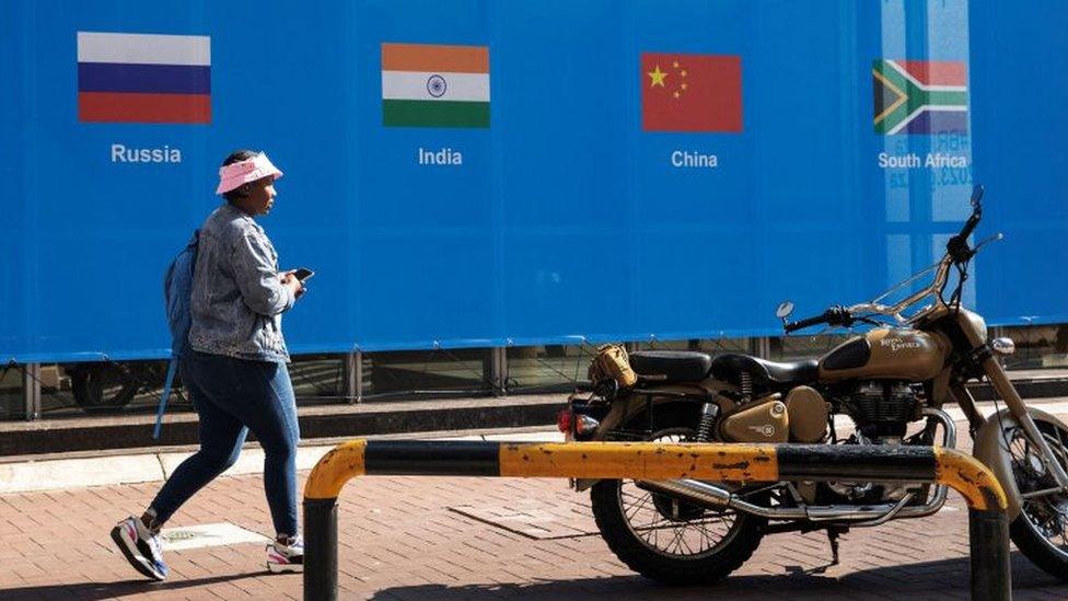 A woman walks past a banner outside the venue for the 2023 Brics summit at the Sandton Convention Centre in Sandton, Johannesburg, on 20 August