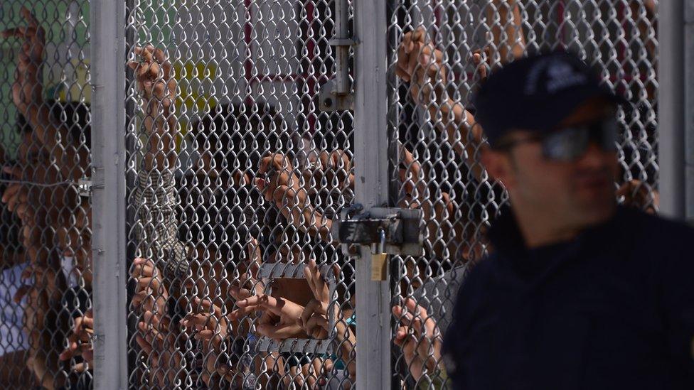 Migrants stand behind a fence in the Moria camp, on the Greek island of Lesbos