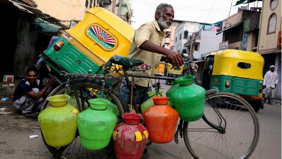 Indian elderly man pushes his bicycle that carry drinking water in plastic pots to deliver to households deprived of drinking water, Bangalore, India, 13th April 2016.