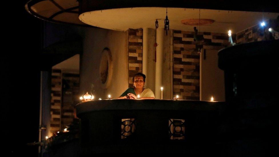 A woman stands on a balcony after lighting an oil lamps in India