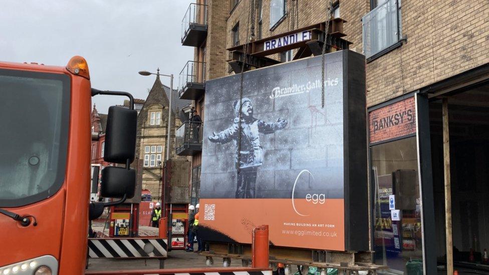 Season's Greetings by Banksy getting craned on to a lorry