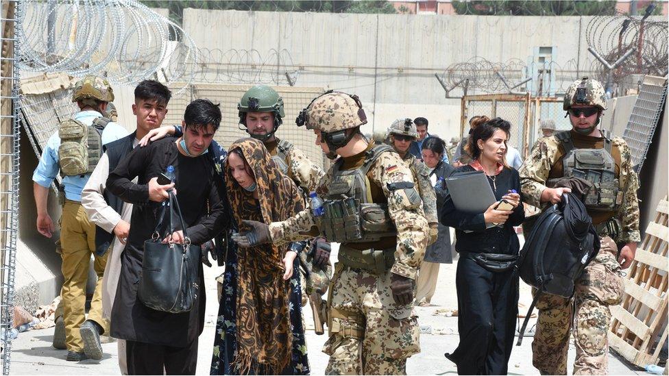 Soldiers help a woman, who fell due to high temperature at the Kabul International Airport as thousands of Afghans rush to flee the Afghan capital of Kabul