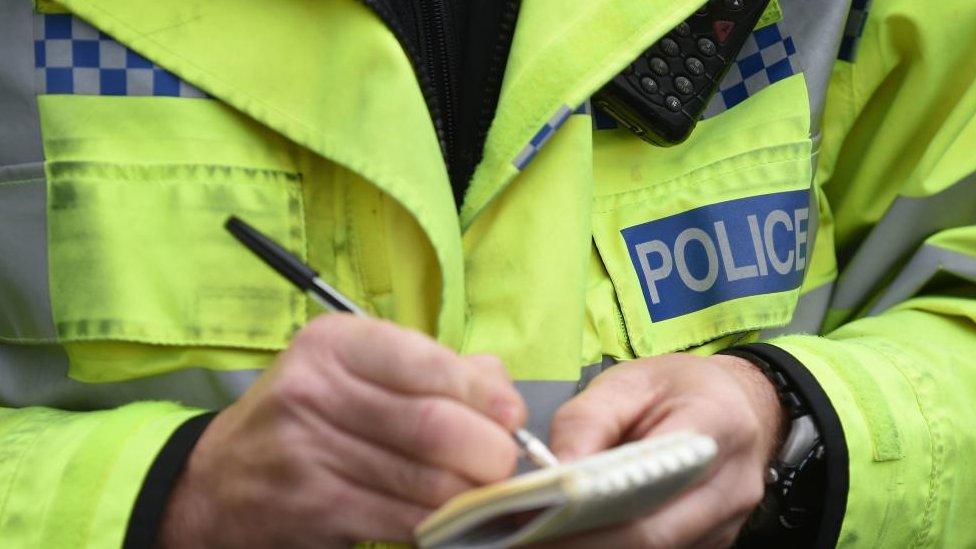 A close-up of a police officer's hands writing in a notepad