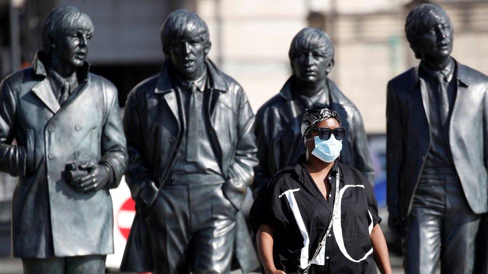 Woman with face mask walks in front of The Beatles statue on Liverpool waterfront