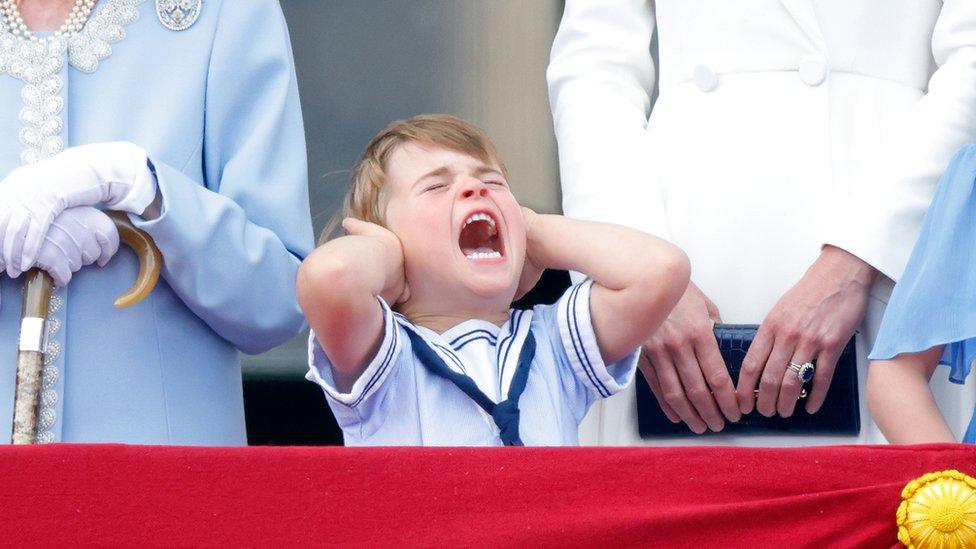 prince louis covers his ears and opens his mouth wide as he tries to cover the noise of the planes flying past