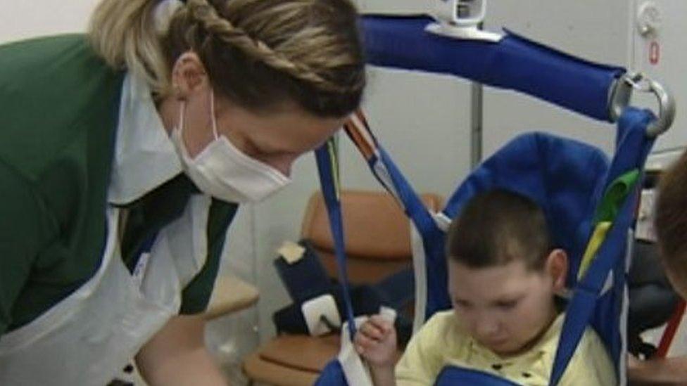 Two female nurses attend to a young boy in a lifting hoist