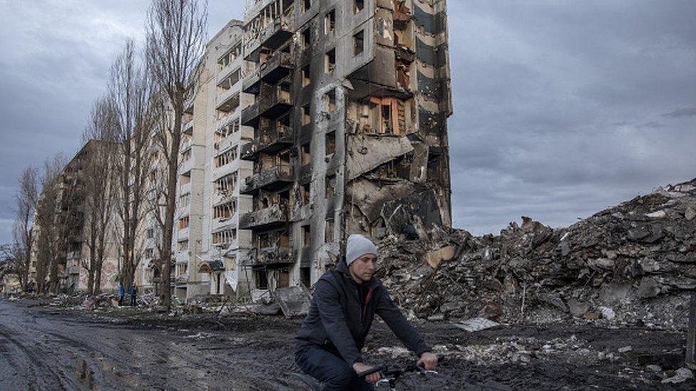 A civilian rides a bike amid destruction on a civilian neighborhood in the town of Borodyanka, on the outskirts of Kyiv,