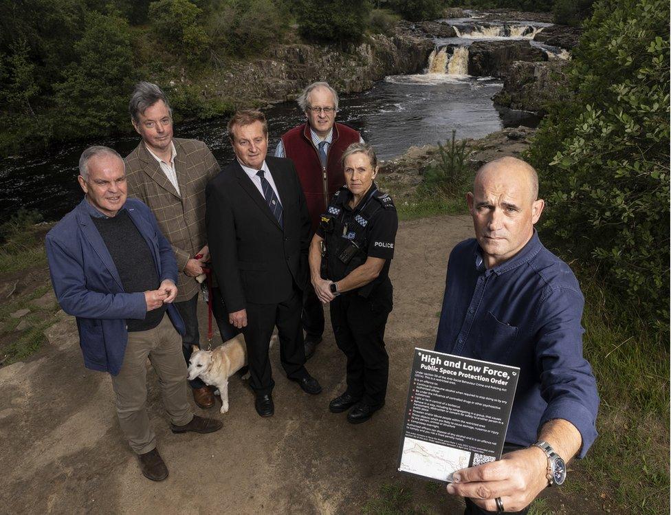 Five council officials and police officer hold a sign detailing the rules next to Low Force waterfall