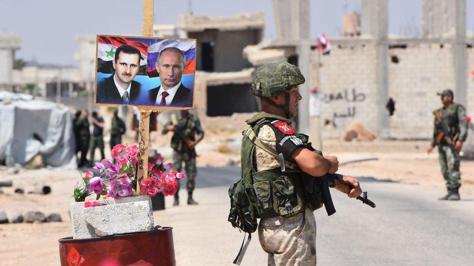 Members of Russian and Syrian forces stand guard near posters of Syrian President Bashar al-Assad and his Russia's Vladimir Putin on the eastern edge of Idlib province on 20 August 2018