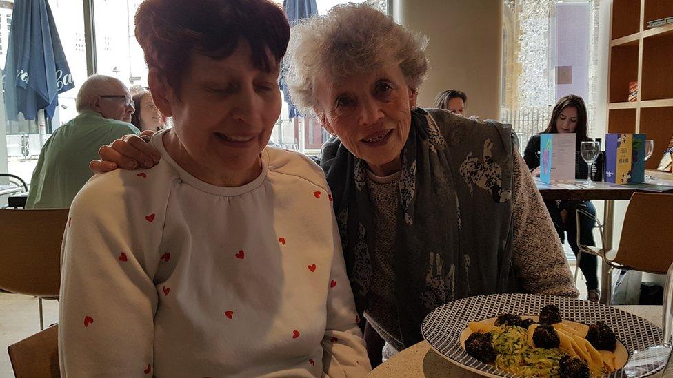 Sylvia Hubbard, right puts her arm around her daughter Jocelyn, Jocelyn is at a table about to eat dinner and both are smiling.