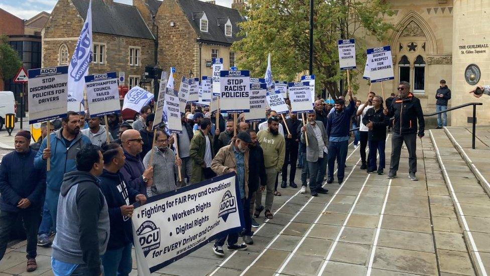 Drivers carrying banners on the steps of a large municipal building