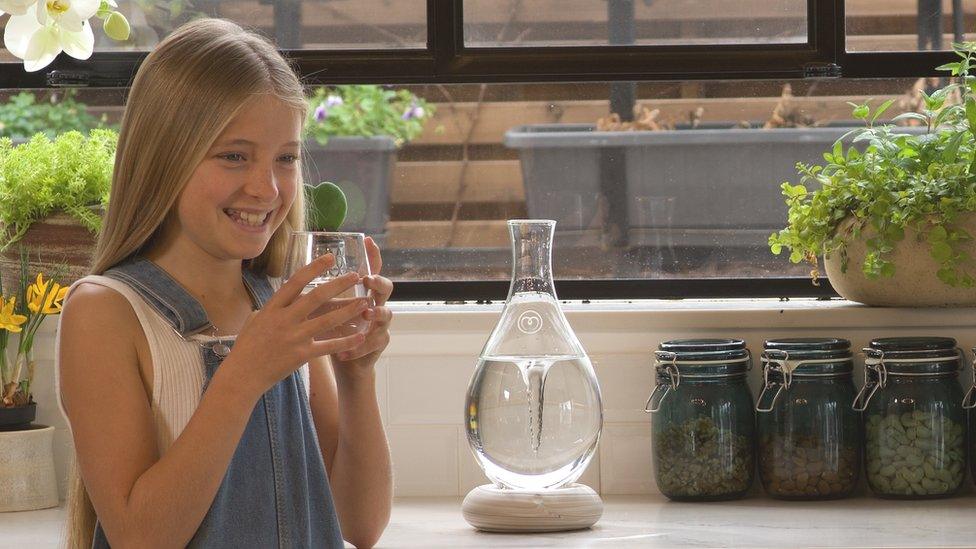 A girl drinking a glass of water from a Mayu machine