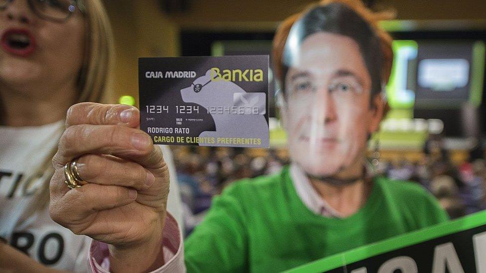 A woman displays a fake Bankia credit card of Rodrigo Rato as she protests against fraud during the Bankia Shareholders Extraordinary General meeting in Valencia on 22 April 2015