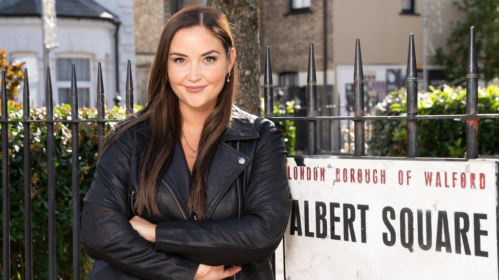 Jacqueline Jossa in front of an Albert Square sign on the EastEnders set