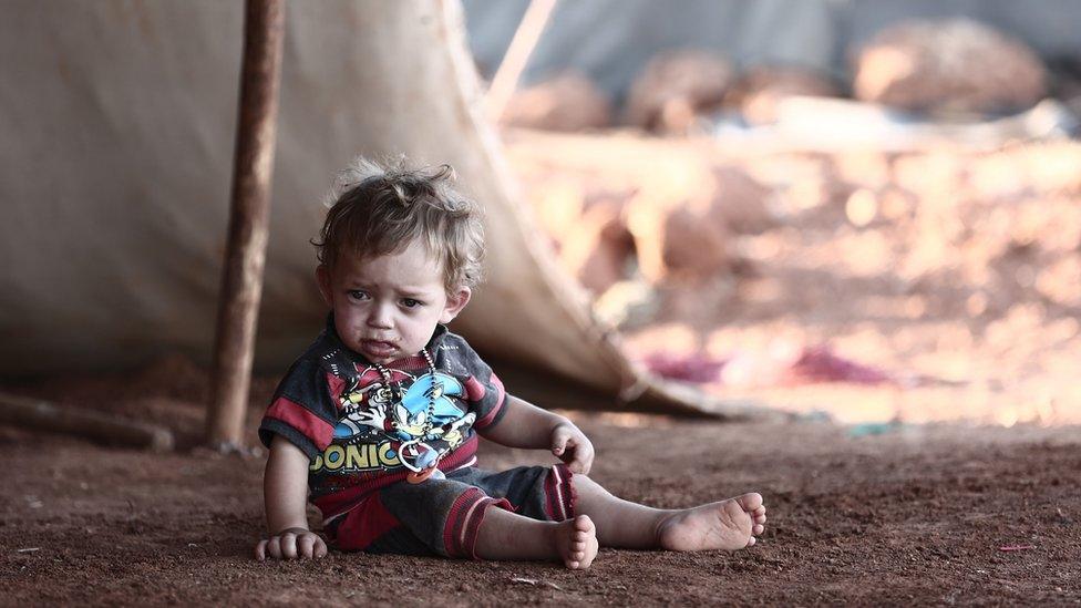 A child sits in front of a tent at a camp for the displaced in the province of Idlib