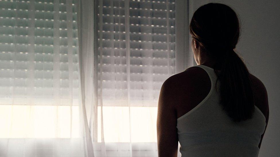 Rear view of an unrecognizable abused woman sitting on her bed looking out the window