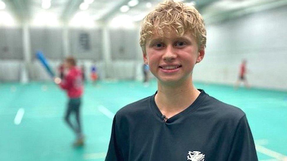 Matthew stands smiling at an indoor cricket court