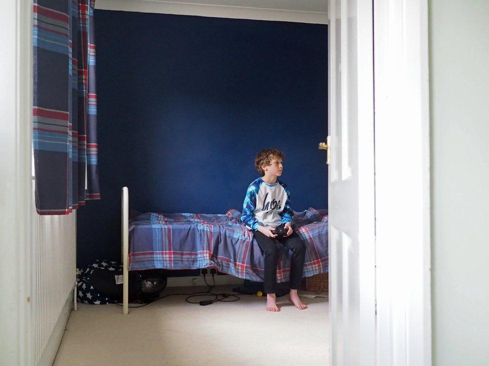 William sitting on his bed, playing computer games