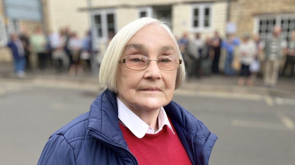 A lady with white hair in red sweater and blue coat