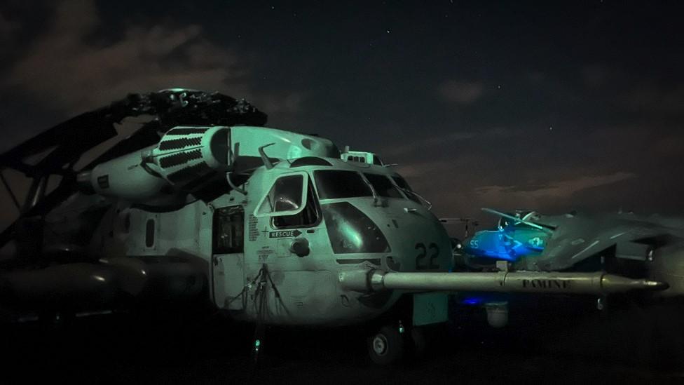 A helicopter and a plane on the ship's deck at night