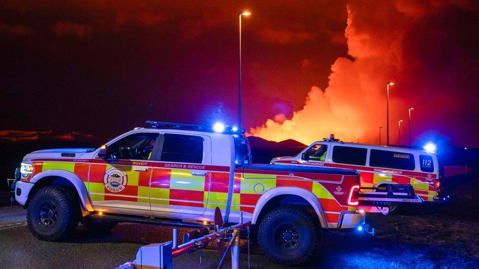 Emergency vehicles are seen as molten lava flows out from a fissure on the Reykjanes peninsula