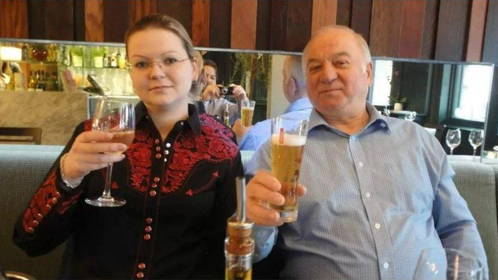 A woman and man sitting next to each other in a restaurant, each holding up a drink.