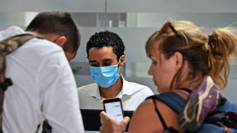 Airline employee with mask and two travellers.