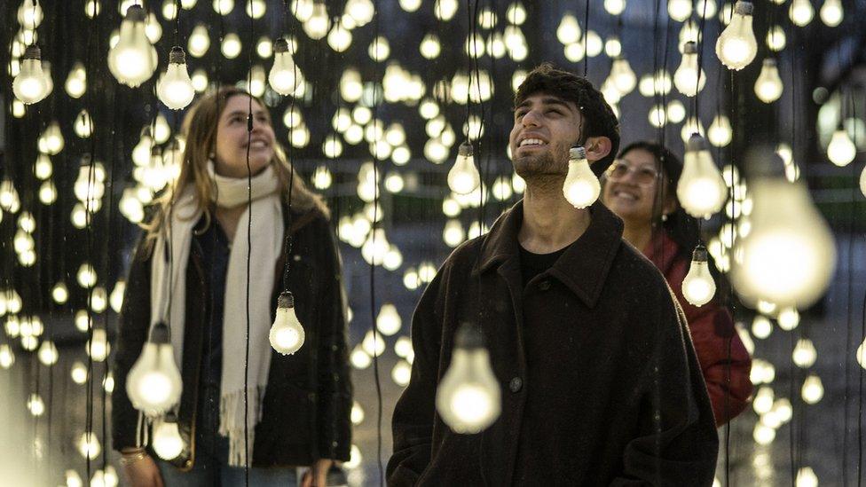 A man and two women stand among lightblubs