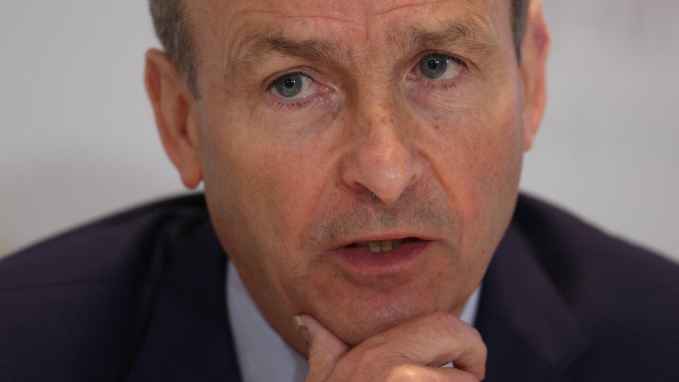 Micheál Martin pictured close up, holding his hand to his chin with a serious expression